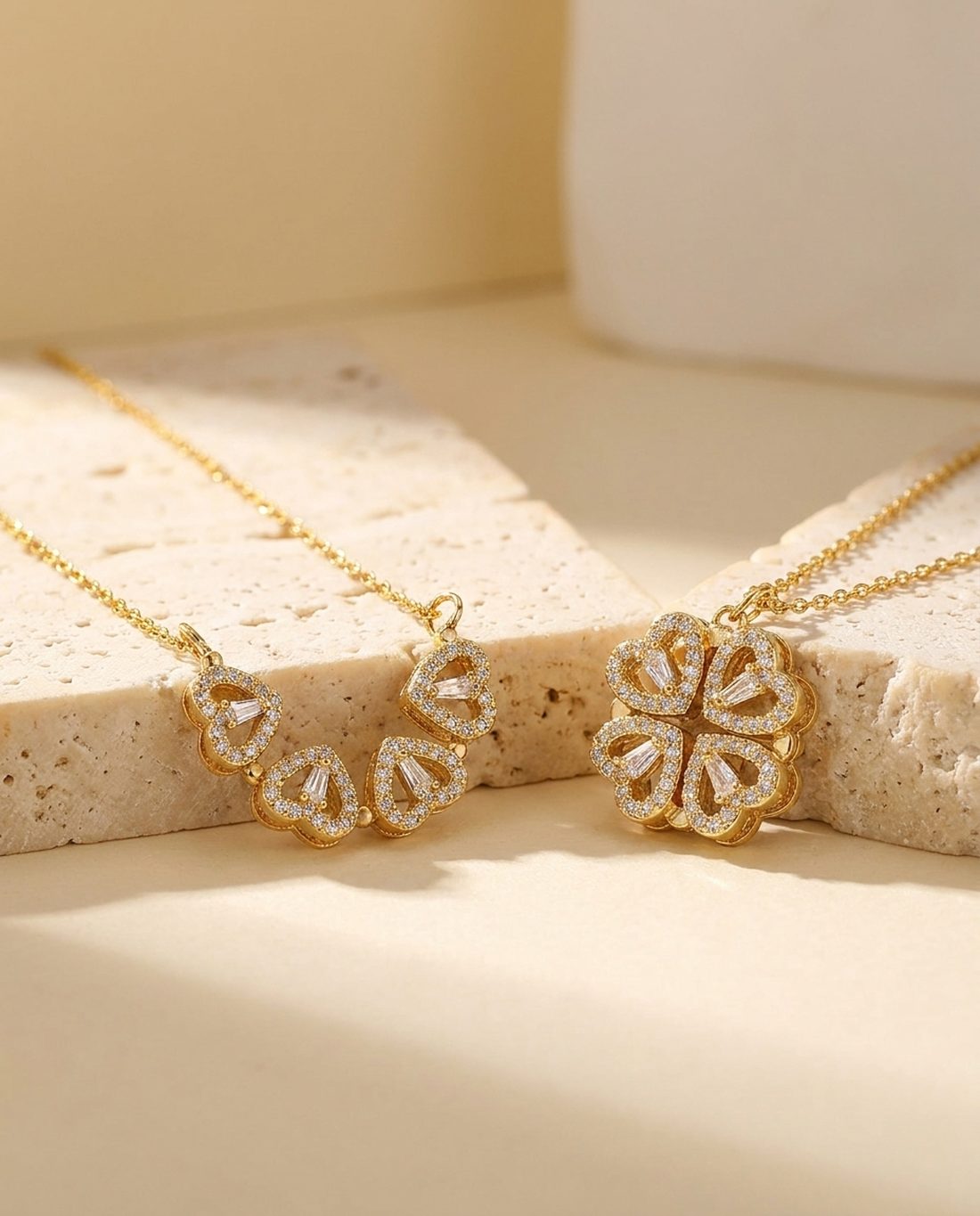 Four leaf clover pendant beside its open four heart form on travertine